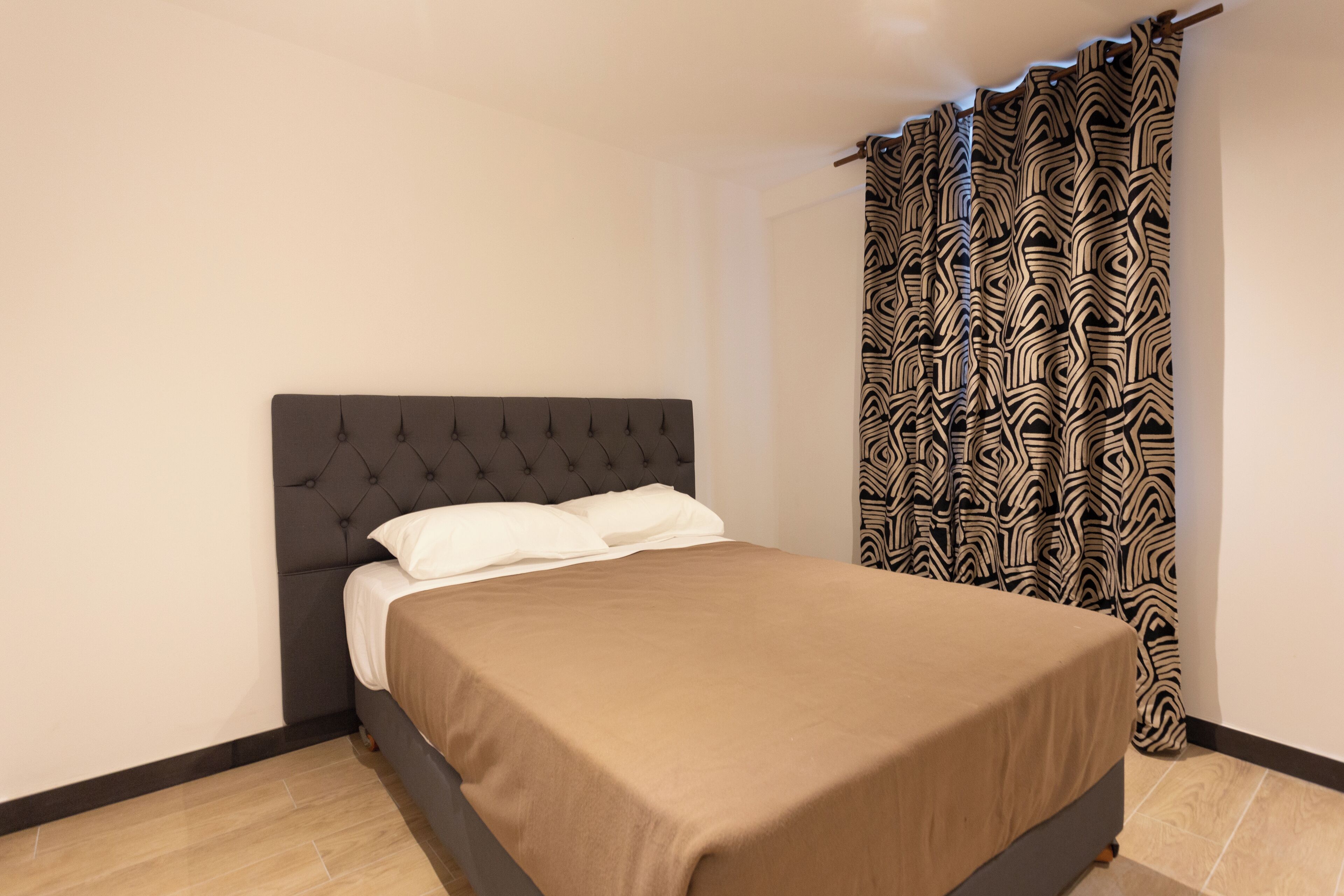A bedroom with a bed, a patterned curtain, and a tiled floor.