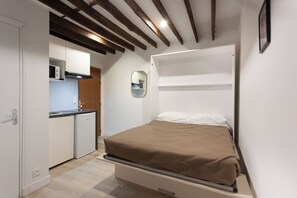 Une petite chambre comprenant un lit, un coin cuisine et un miroir au mur.
