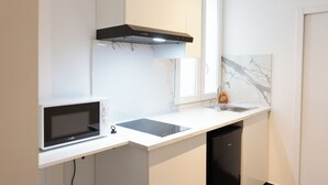 Une cuisine moderne avec des meubles blancs, un micro-ondes noir, un four encastré, un lave-vaisselle noir et un pare-feu en marbre.