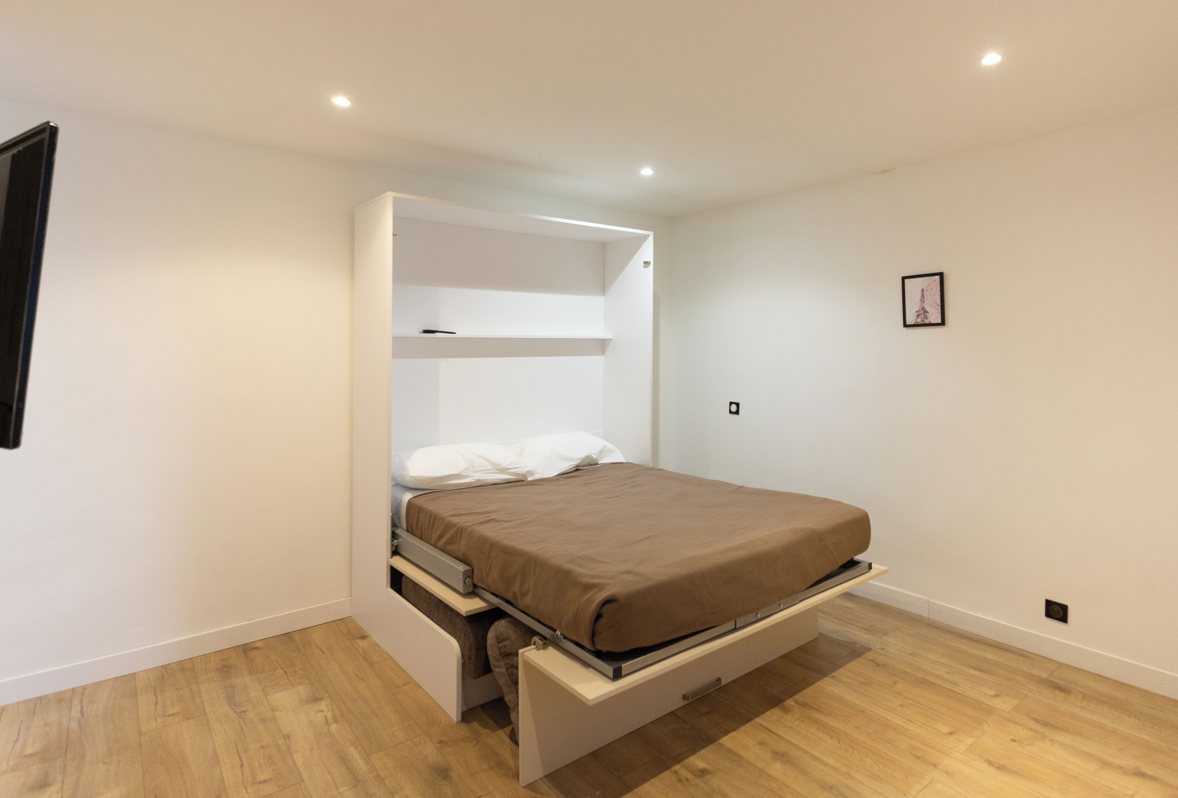 A bedroom with a bed, built-in storage, and a wooden floor.