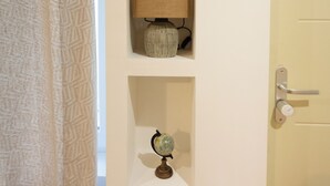 Une porte avec un interrupteur et une poignée, un mur blanc avec trois étagères et un rideau à motifs.