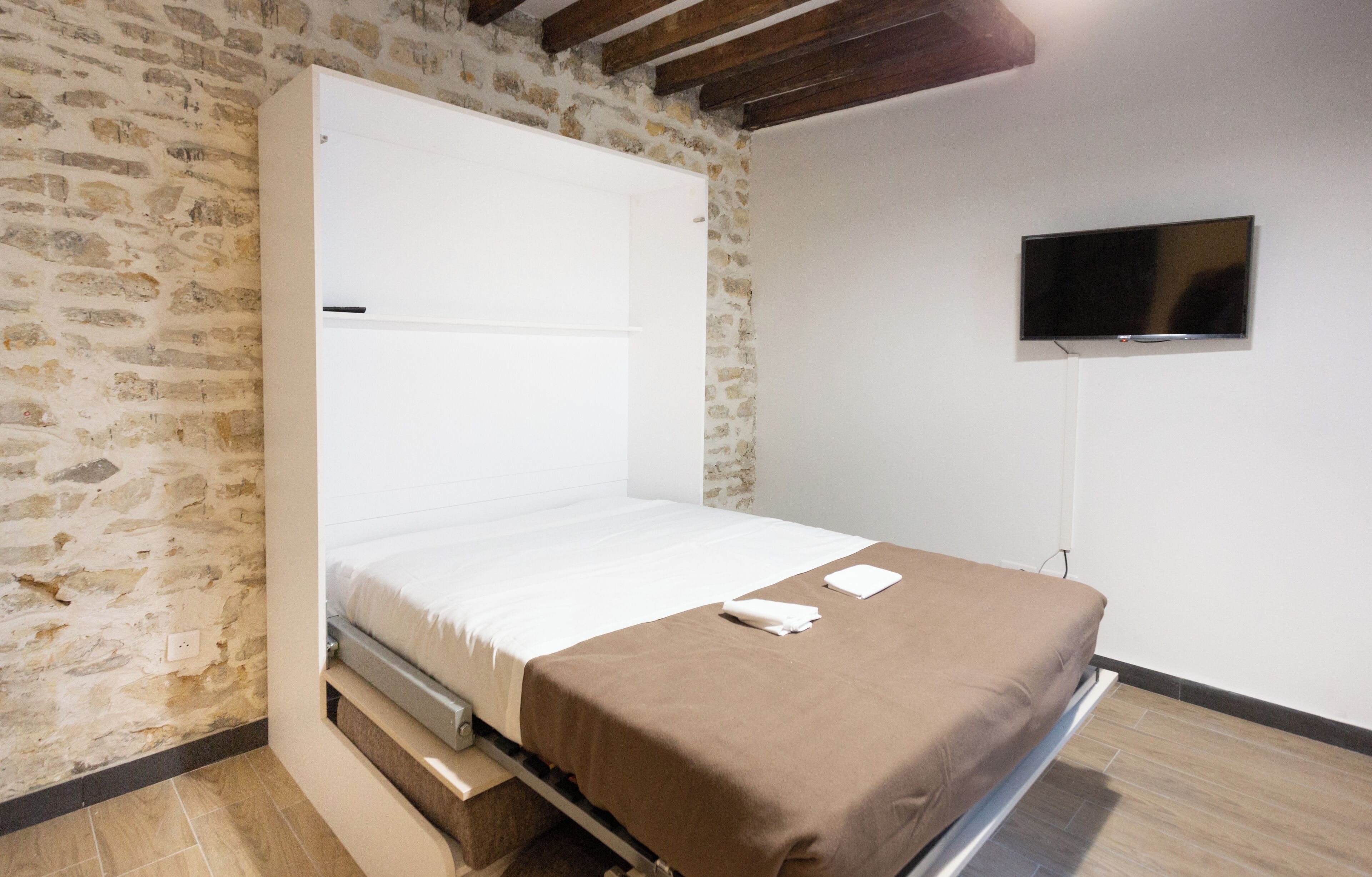 Een slaapkamer met een bed, een aan de muur bevestigde televisie en een stenen muur.