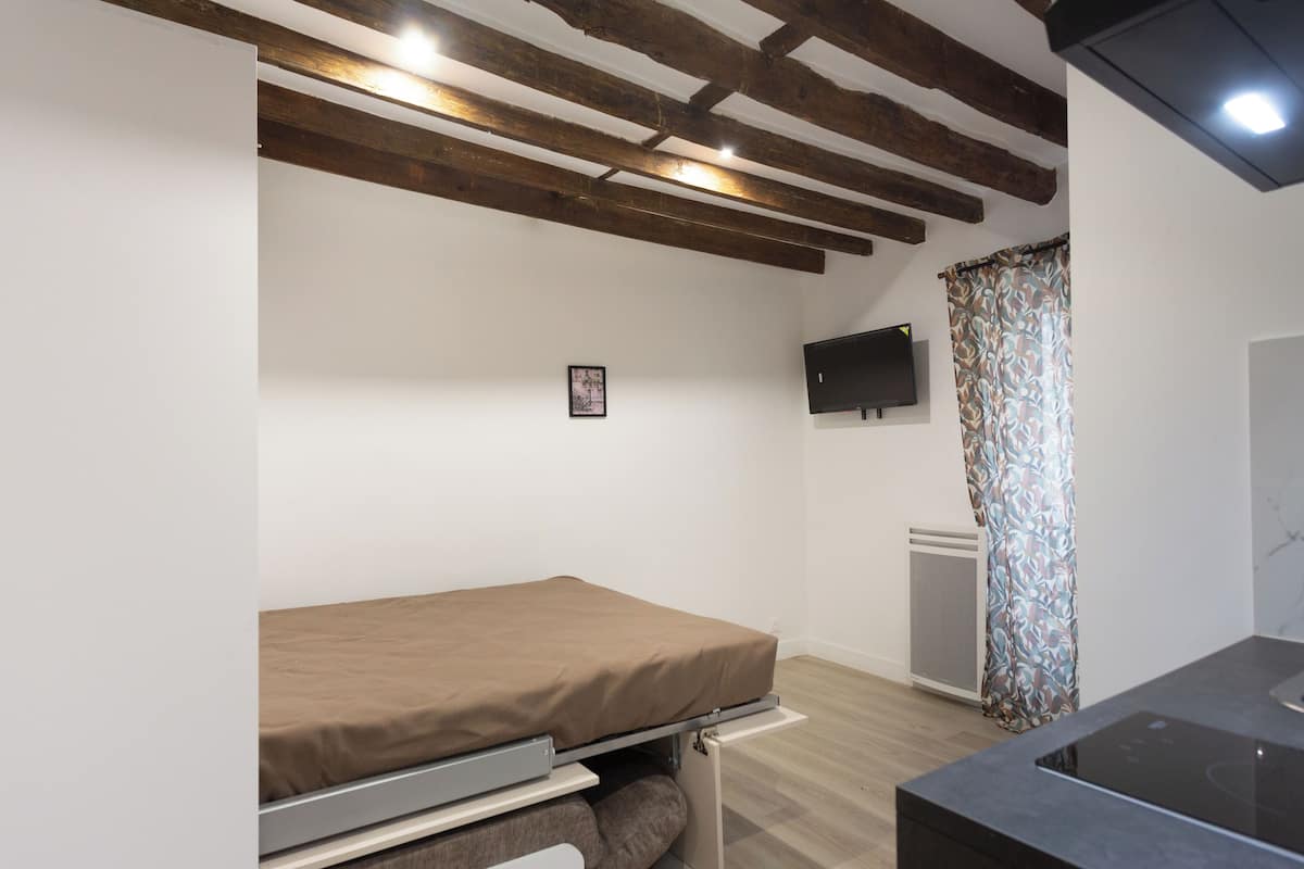Une chambre de taille modeste, équipée d’un lit, d’un téléviseur fixé au mur et d’un petit coin cuisine.