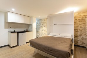 Une chambre avec un lit, un petit coin cuisine et un mur en pierre.