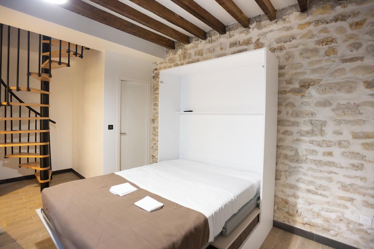 Une chambre à coucher avec un lit, un escalier en bois et un mur en pierre.