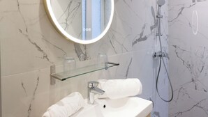 Une salle de bain moderne avec un pare-baignoire en marbre, un miroir rond, une étagère en verre, un lavabo blanc, une serviette et une douche.