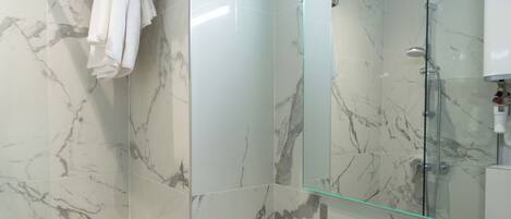 A modern bathroom with marble walls, a glass shower enclosure, a white sink, and a towel rack.