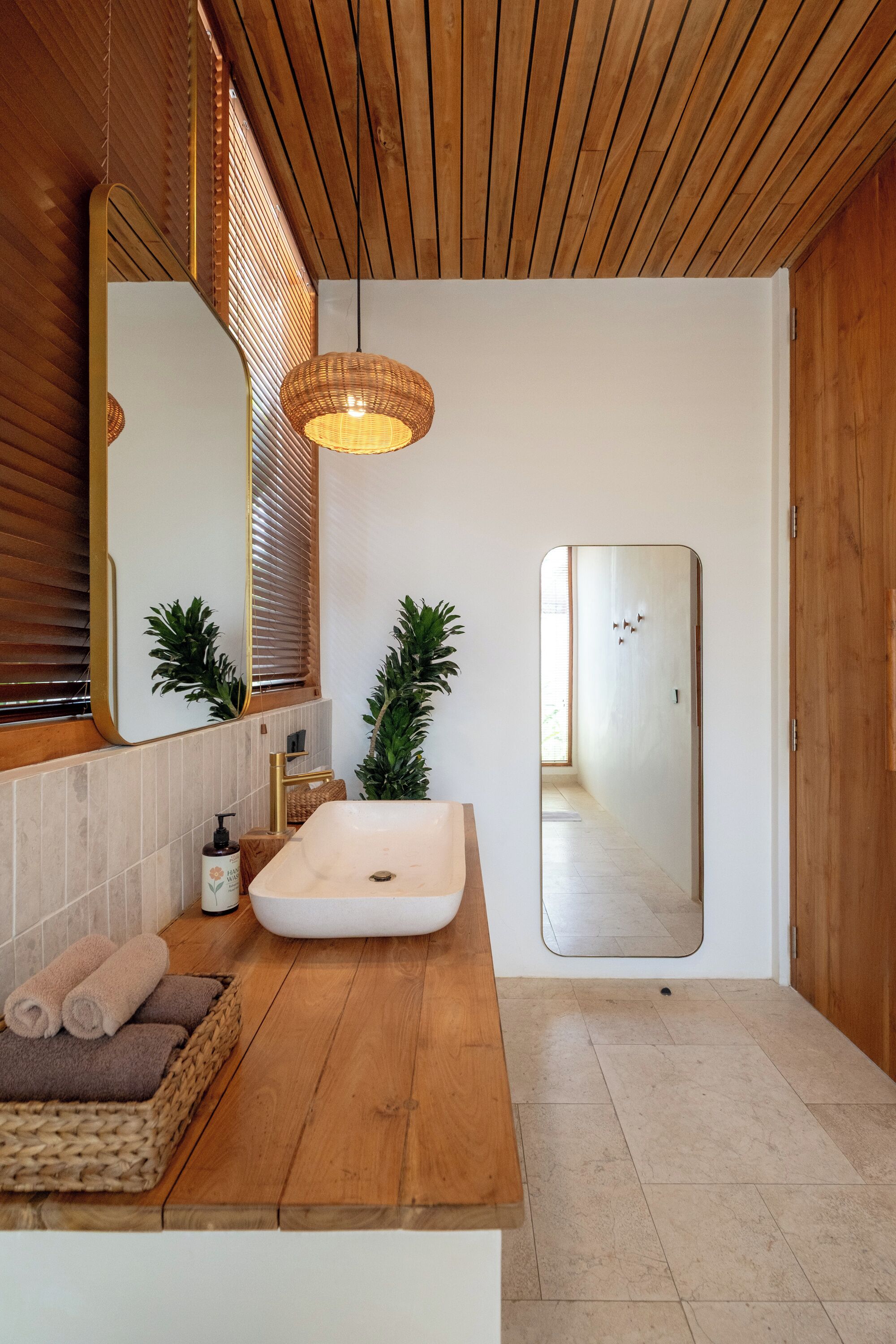 A modern bathroom with a wooden ceiling, a large mirror, a white sink, and a wooden floor.