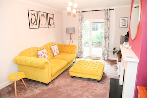 A bright yellow sofa with a matching ottoman, a small side table, and a floor lamp.