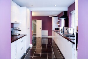 Une cuisine moderne avec des meubles blancs, un sol carrelé noir et un mur d’accent violet.