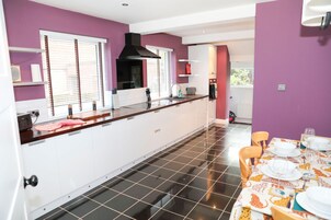 Une cuisine moderne avec des meubles blancs, une hotte noire et un coin repas avec une table dressée pour quatre personnes.