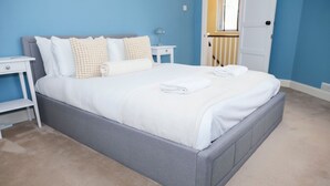 Un letto rifatto con lenzuola bianche e una testiera grigia in una stanza con pareti blu e tappeto beige.