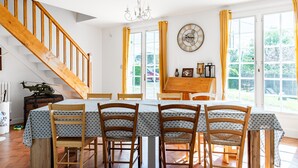 A dining area with a wooden staircase, a chandelier, and a large window with curtains.