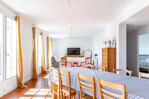 Uma área de refeições com mesa posta para quatro pessoas, televisão e um armário com objetos decorativos.