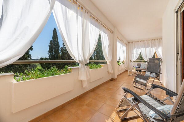 A balcony with white curtains, a tiled floor, and a seating area with chairs and a table.