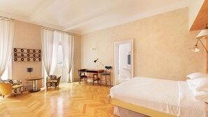 Ein Hotelzimmer mit einem großen Bett, einem Schreibtisch, zwei Stühlen, einem kleinen Tisch und einer Lampe.