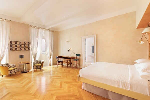 A hotel room with a large bed, a desk, two chairs, a small table, and a lamp.