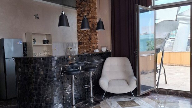 A modern kitchen with a central island, black bar stools, and a white chair. - 3-bedroom apartment in Batumi (Batumi)