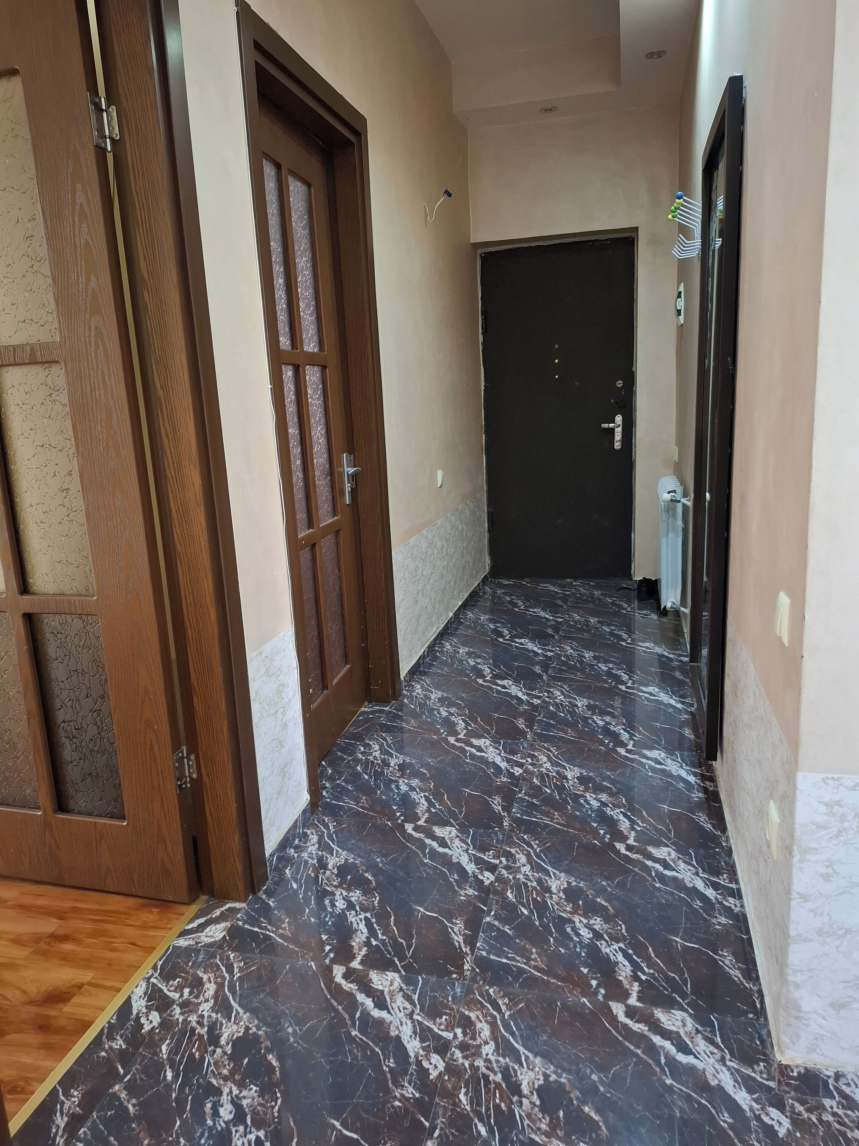 A hallway with a marble floor, wooden doors, and a black door at the end.
