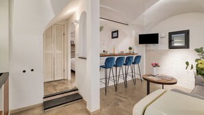 A modern kitchen with a bar area, white walls, and a TV mounted on the wall.