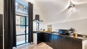A modern kitchen with black cabinets, a herringbone wood floor, and a large window with black curtains. - Boutique Apartment Casa Del Barone (Ventimiglia)