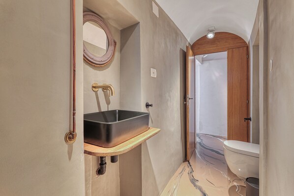 A narrow bathroom with a wooden vanity, a black sink, and a white toilet. - Boutique Apartment Casa Del Nobile (Ventimiglia)