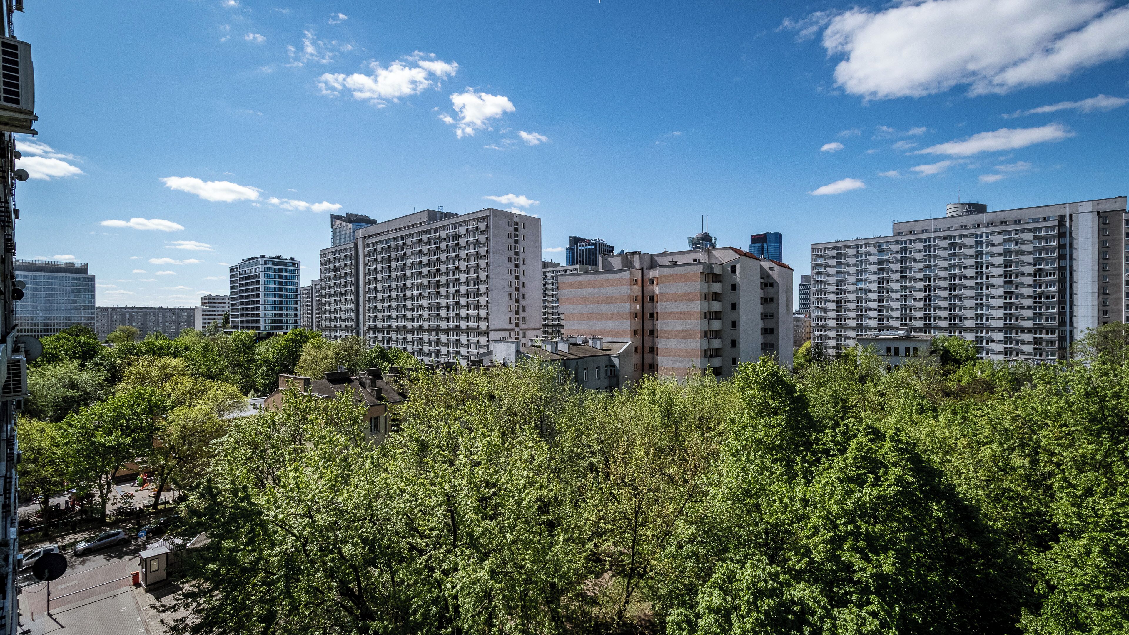 A cityscape with high-rise residential buildings, dense greenery, and a clear blue sky.