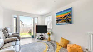 A modern living room with a sofa, a flat-screen TV, a painting, and a view of the backyard. - Castle Park is a fantastic gem of a property located in Paignton. (Paignton)