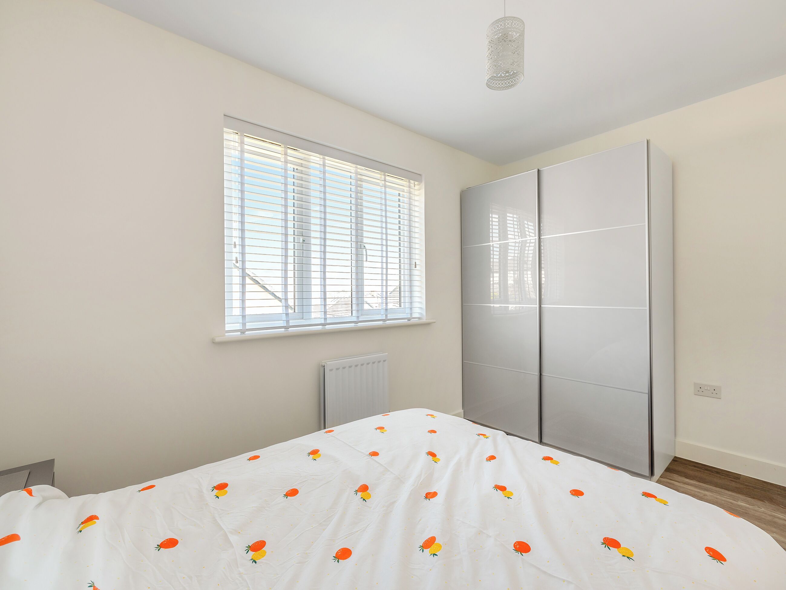 A bedroom with a bed, a window with blinds, a radiator, and a wardrobe.