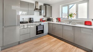 A modern kitchen with grey cabinets, a built-in oven, a microwave, and a red toaster. - Castle Park is a fantastic gem of a property located in Paignton. (Paignton)