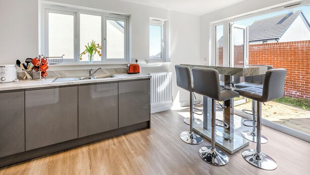 A modern kitchen with a large island, a dining area with bar stools, and large windows providing natural light. - Castle Park is a fantastic gem of a property located in Paignton. (Paignton)
