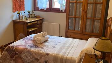 Un dormitorio con dos camas, un armario de madera, un escritorio con silla, un radiador y una ventana con cortinas.