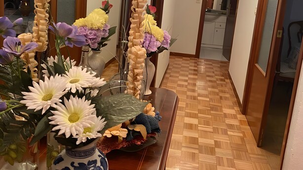 Ein Flur mit Holzboden, einer Blumenvase und einem Spiegel an der Wand.
