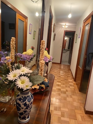 Un pasillo con piso de madera, un jarrón con flores y un espejo en la pared.