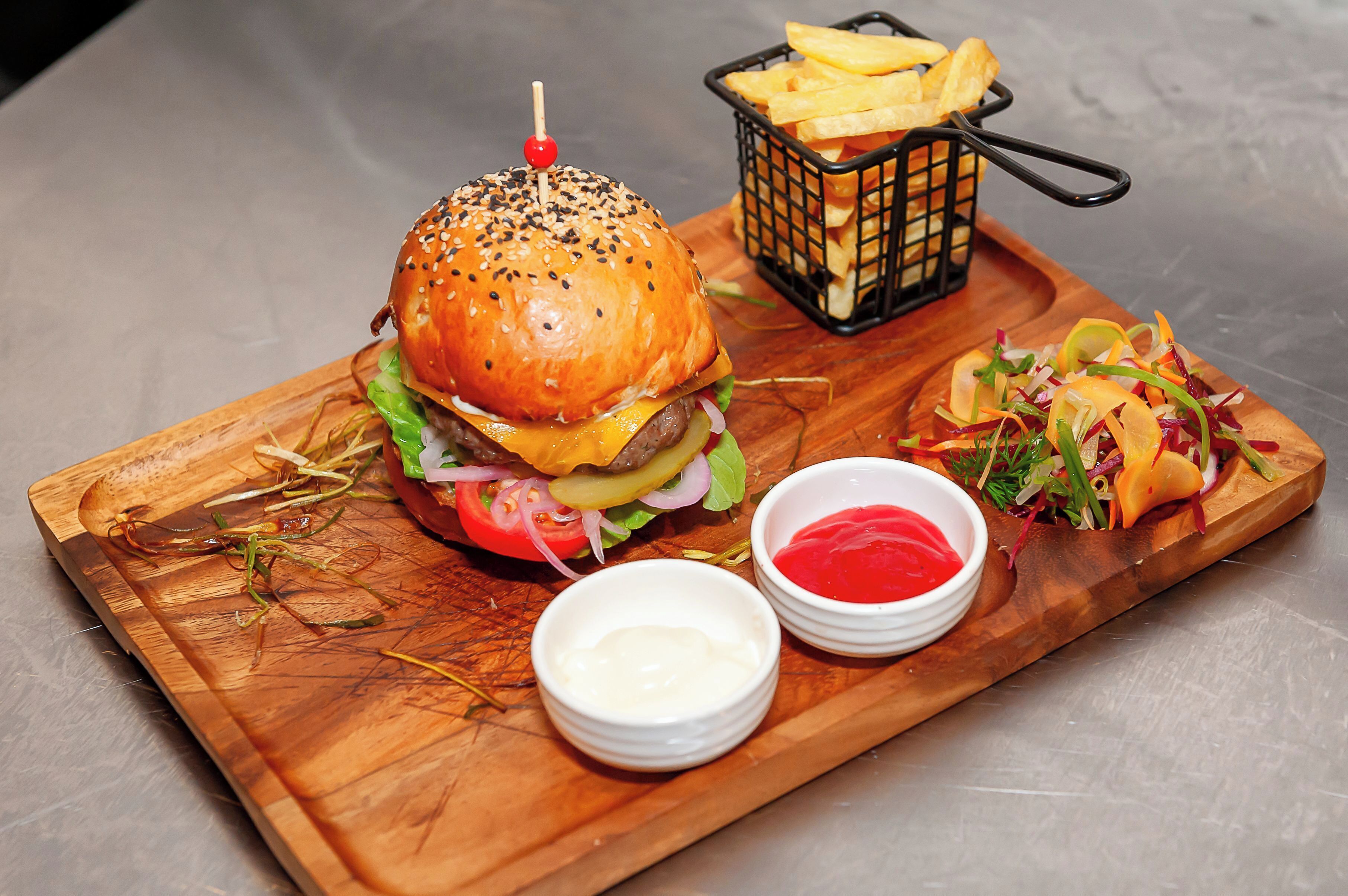 Una tabla de madera con una hamburguesa, papas fritas y una ensalada.