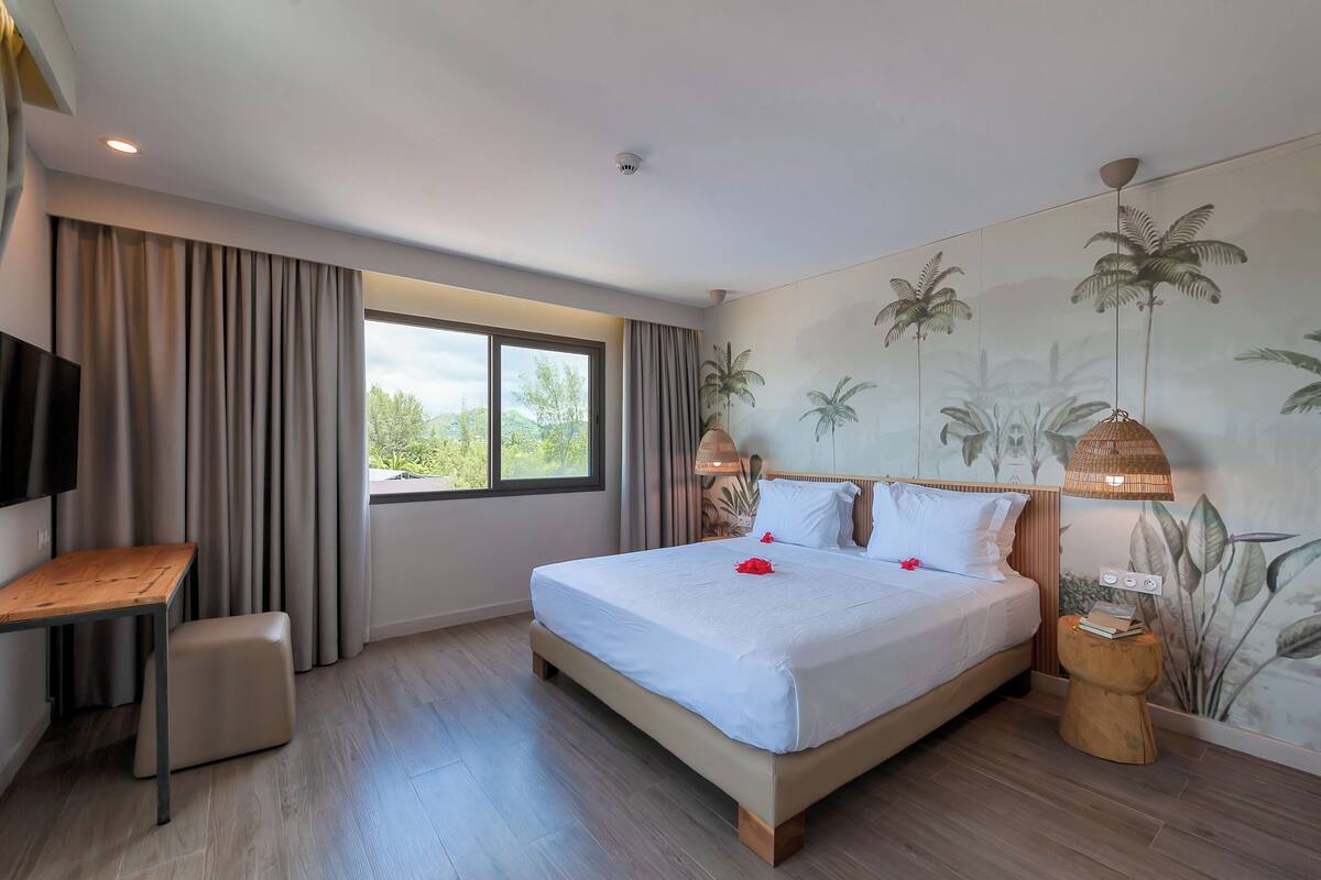 Ein modernes Hotelzimmer mit einem großen Bett, einem Schreibtisch und einem Fenster mit Vorhängen.