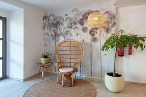 Una habitación con una silla de ratán, una planta grande en maceta, un mural en la pared y una lámpara colgante.