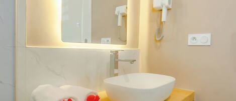 A bathroom with a white sink, a mirror, a towel with red flowers, and a hairdryer on the wall.