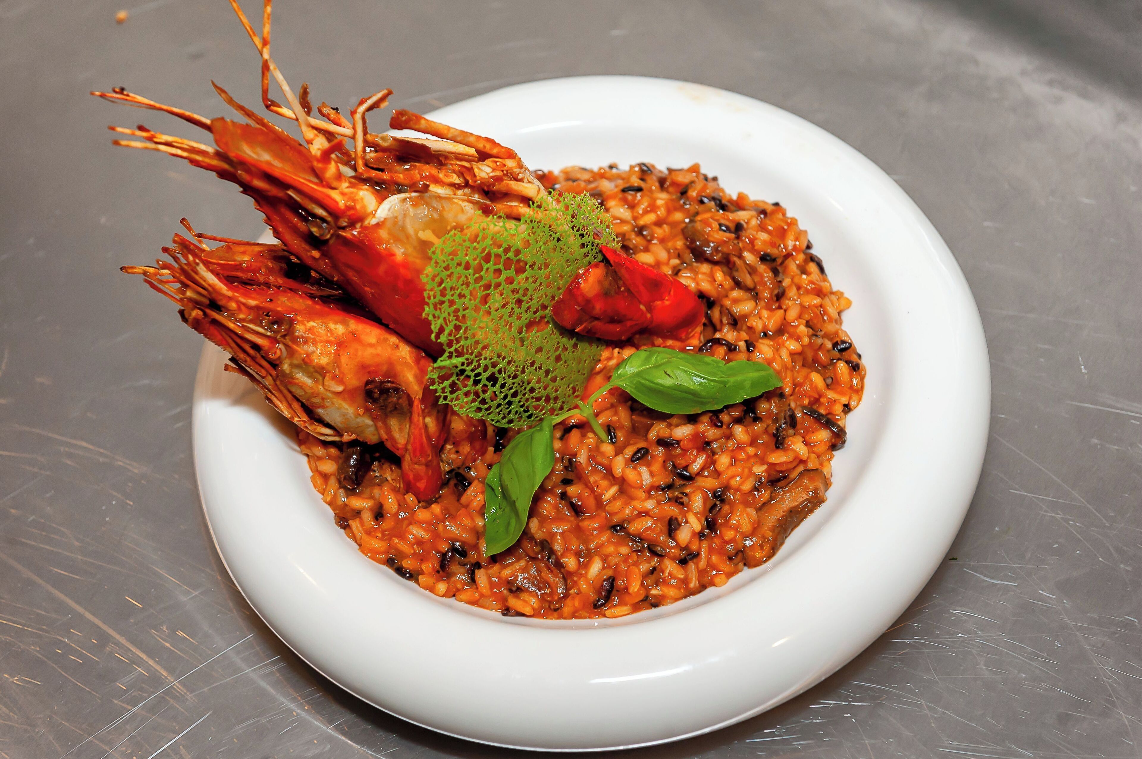 Un plato de risotto de mariscos con camarones y una guarnición verde decorativa.