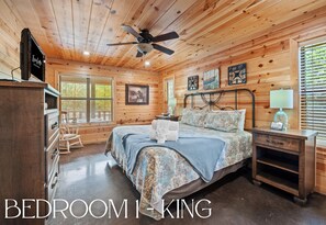 A wooden-paneled bedroom with a bed, bedside tables, a ceiling fan, and artwork on the walls. - Playset | Outdoor Games | Hot Tub | Fire Pit (Broken Bow)