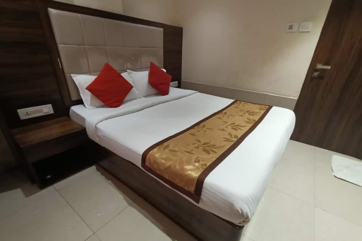 Una cama bien hecha con una colcha blanca y dorada, dos almohadas rojas y un cabecero de madera.