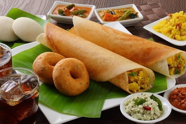 A meal with a variety of dishes including a rolled flatbread, a bowl of yellow rice, and several small bowls of different sauces.