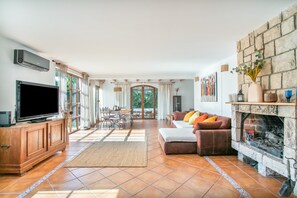 A spacious living room with a flat-screen TV, a stone fireplace, and a dining area with a table and chairs. - Holiday Home 'Beniarbeig' with Mountain View, Wi-Fi and Air Conditioning (El Campello)