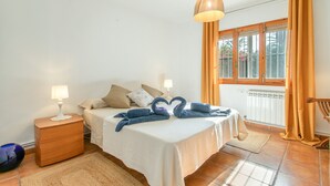 Un dormitorio con cama, mesitas de noche, lámpara, ventana con cortinas y vistas a palmeras.