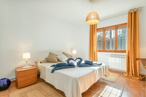 A bedroom with a bed, nightstands, a lamp, a window with curtains, and a view of palm trees. - Holiday Home 'Beniarbeig' with Mountain View, Wi-Fi and Air Conditioning (El Campello)