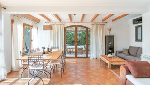 A spacious living area with a dining table, chairs, a sofa, and a view through a glass door to an outdoor patio. - Holiday Home 'Beniarbeig' with Mountain View, Wi-Fi and Air Conditioning (El Campello)