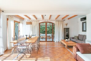 A spacious living area with a dining table, chairs, a sofa, and a view through a glass door to an outdoor patio. - Holiday Home 'Beniarbeig' with Mountain View, Wi-Fi and Air Conditioning (El Campello)