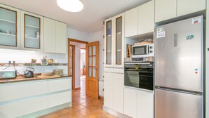 Una cocina con gabinetes blancos, microondas, horno y refrigerador.