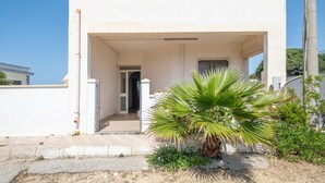 Un edificio blanco con un porche cubierto, una palmera y un pequeño jardín.