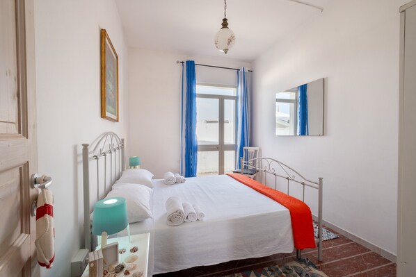 Habitación de hotel con cama, mesita de noche, lámpara, espejo y ventana con cortinas.